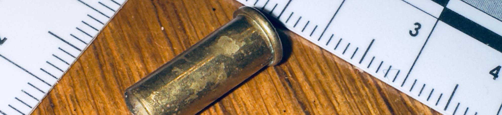 ruler next to a bullet casing on a wood floor
