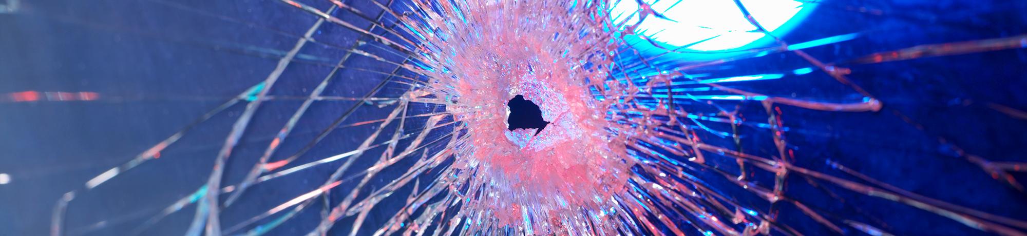 a bullet hole in a windshield with police lights in the background