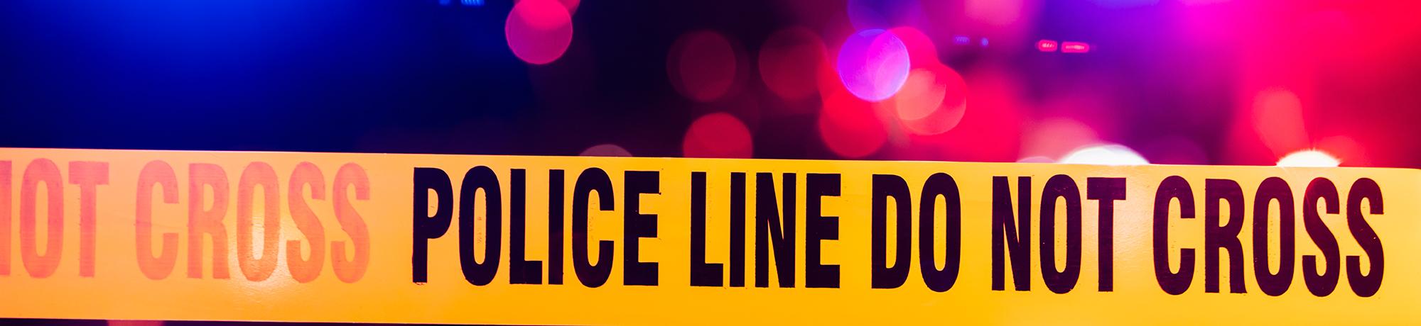 police tape at a crime scene with police lights in the background